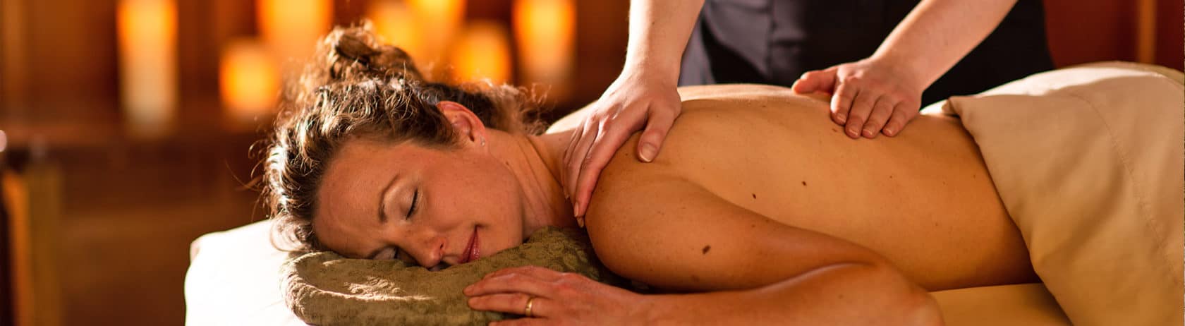 An image of a woman lying on a massage table with a smile, eyes closed, and receiving a relaxing stress-relief massage at a spa.