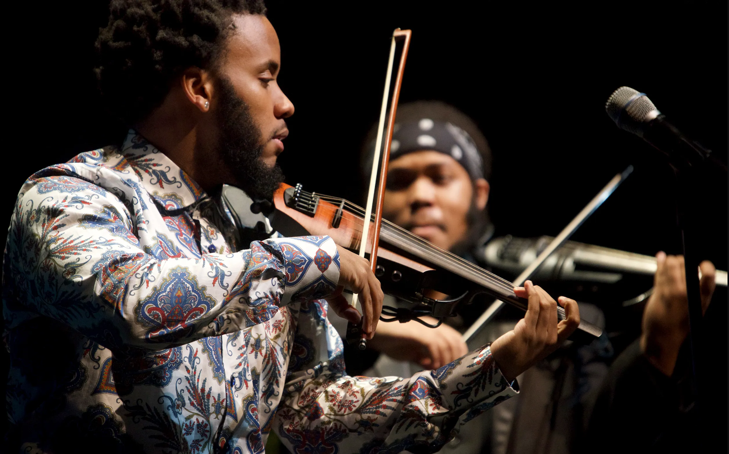 Image of Sons of Mystro Duo playing the violin in front of a microphone