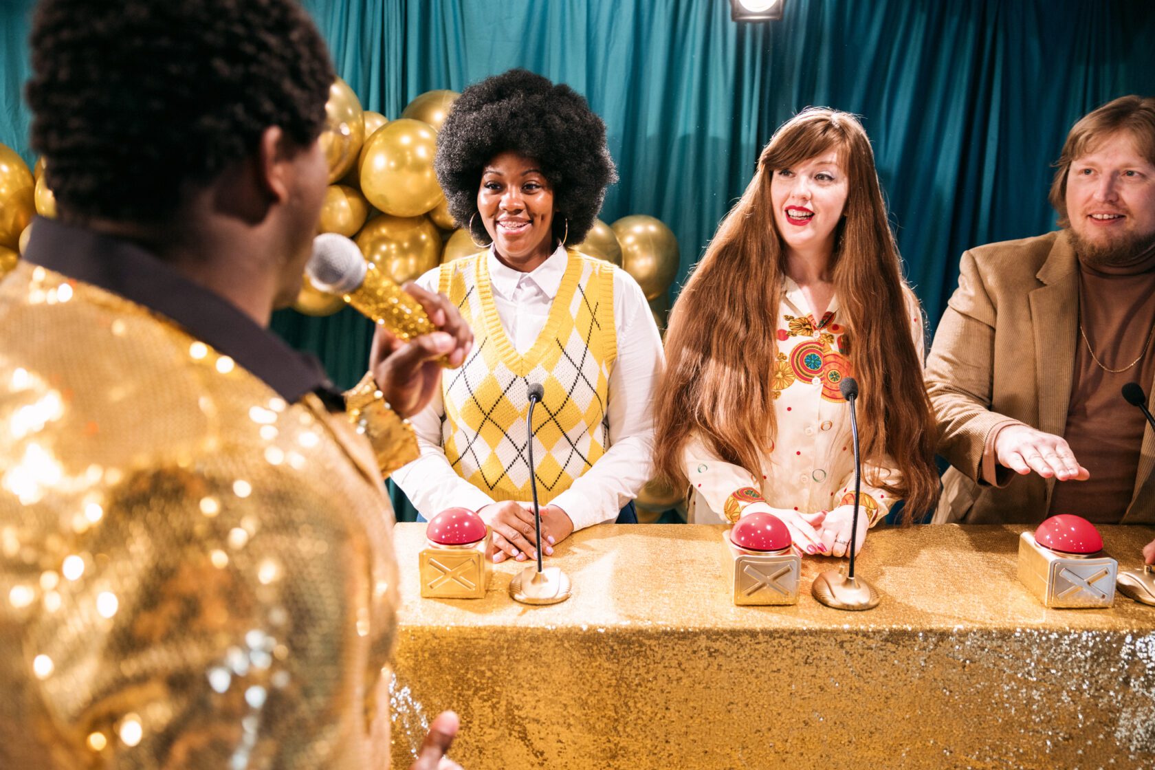 A fun depiction of a competitive TV game show, stylized in late 1970's or early 1980's fashion.  The host, an African American man in a stunning gold blazer, asks the contestants quiz trivia questions to see who will win the grand prize!  The participants hold their hands over their buzzers to signal they have the answer.